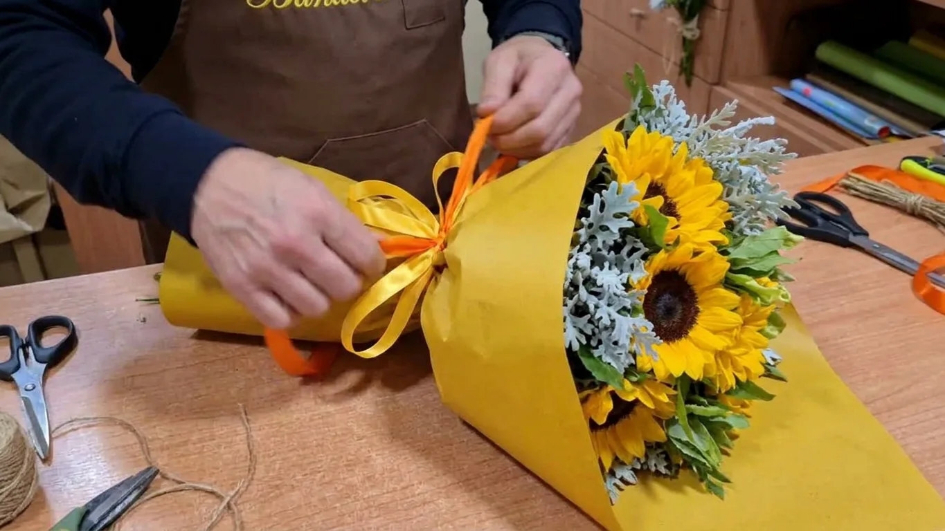 Le mani di Marco che rifiniscono un bouquet di girasoli con incarto personalizzato nel negozio di fiorista Bandera
